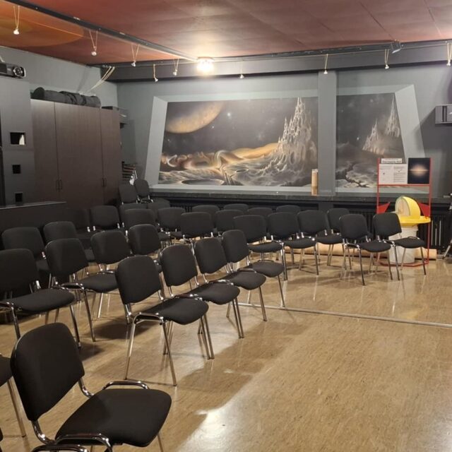 Vortragssaal der Sternwarte Hof mit Stuhlreihen, Projektor und astronomischer Wandgestaltung
